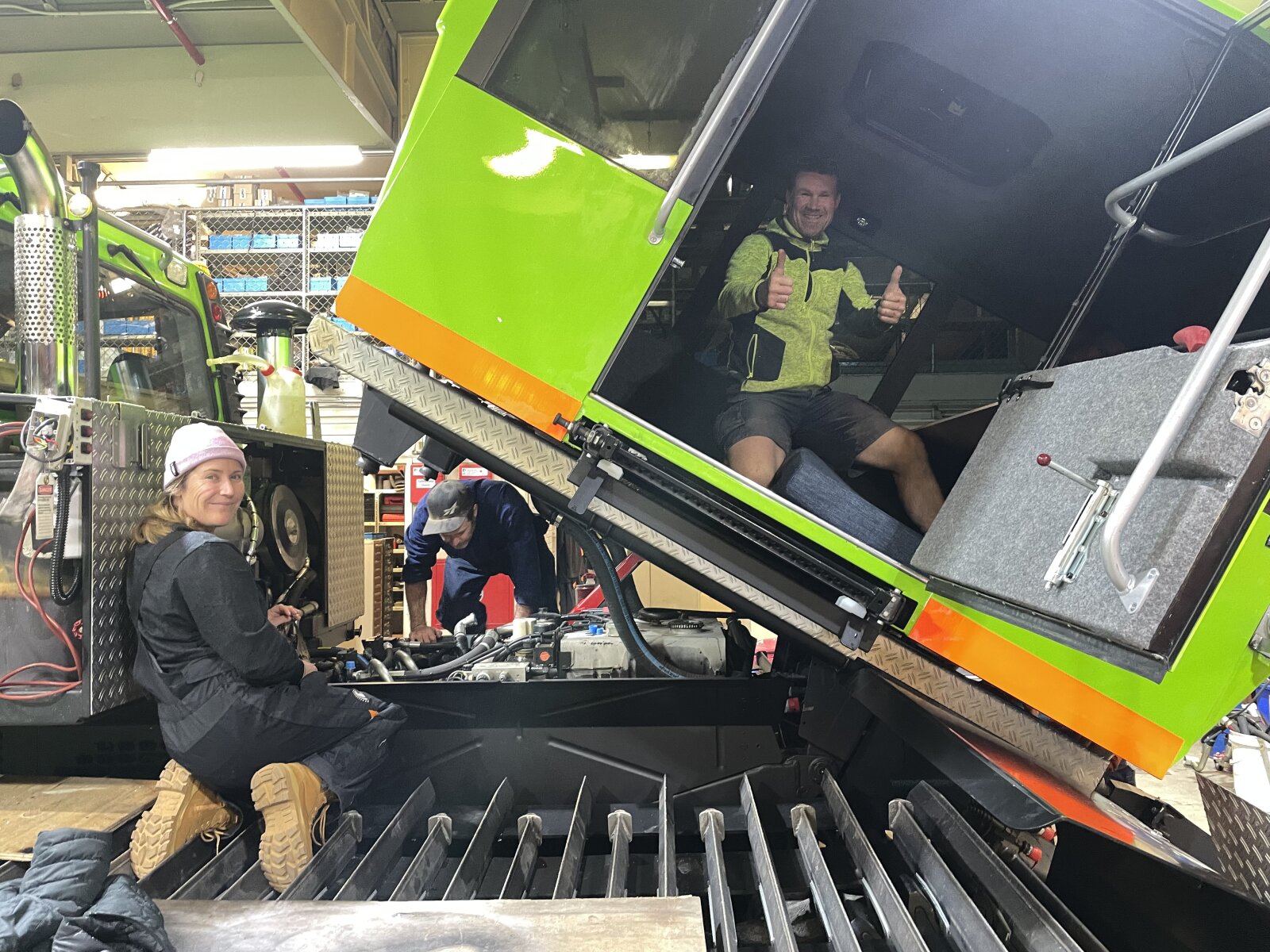 Three people
working on a PistenBully PB300 Polar, with the passenger compartment raised